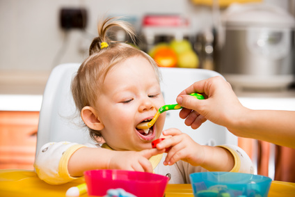 Child girl eats porridge from a spoon on kitchen.